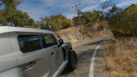 speed-drone-shot-of-Military-grade-truck,-grey-Rezvani-Tank-rear-cinematic-closeup-view-on-rough-road-in-arid-mountain-area-covered-with-trees