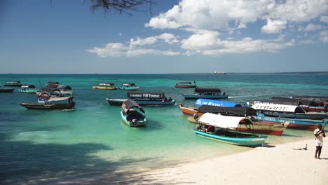 Tour-boats-stationed-and-being-loaded-off-with-tourists-and-locals-on-sandy-shore,-Locked-wide-shot