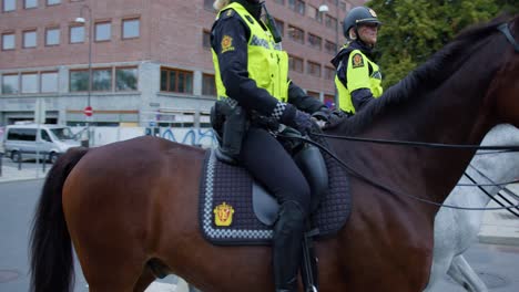 Two-happy-police-officers-women-riding-and-waving-to-camera-in-Oslo-downtown