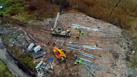 Crew-putting-together-an-electrical-transmission-tower-along-a-countryside-road-in-Latvia---pull-back-aerial-view