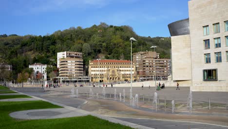 Fountain-waterspouts-in-front-of-Guggenheim-Museum-with-people-far-away,-Wide-shot