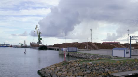 Cargo-ship-in-seaport-full-of-timber-log-piles,-daytime,-wide-shot,-camera-moves-left