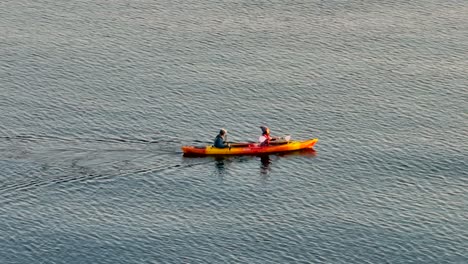 Cerrar-La-Vista-Aérea-De-Drones-De-Una-Pareja-Joven-Divirtiéndose-En-Un-Kayak-De-Mar-Remando-En-Una-Bahía-Cerca-De-Seattle,-Washington,-Justo-Después-Del-Amanecer-En-La-Mañana