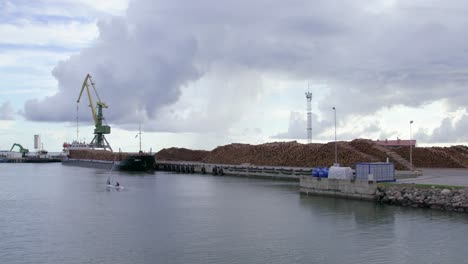 Cargo-ship-in-seaport-full-of-timber-log-piles,-daytime,-wide-shot,-camera-moves-in