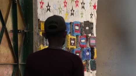 Baseball-Cap-Wearing-Male-Walking-Along-Wall-With-Coloured-Tiles-In-Malir