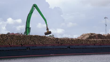 La-Grúa-Carga-Troncos-De-Madera-En-Un-Buque-De-Carga-Lleno-De-Troncos-De-Madera-En-El-Puerto-Marítimo,-Plano-Estático-Y-Amplio