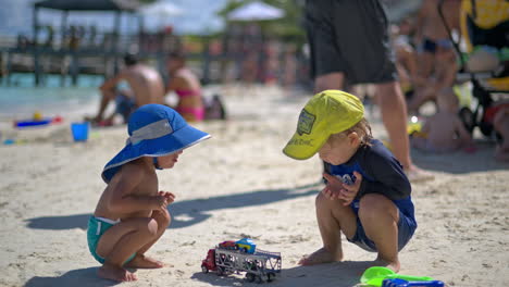 Two-young-babies-from-different-ethnicities-playing-at-the-beach-with-car-toys-on-a-hot-summer-day