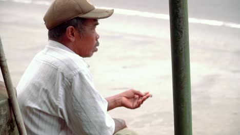 Video-En-Cámara-Lenta:-Toma-De-Cerca-Del-Pobre-Hombre-Sentado-Al-Lado-De-La-Carretera-Y-Fumando-Cigarrillo,-Vista-Lateral-De-Cerca