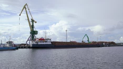 Buque-De-Carga-En-El-Puerto-De-Madera-Lleno-De-Troncos-Cargados-En-El-Barco-Por-Grúa,-Tiro-Estático,-Ultra-Amplio