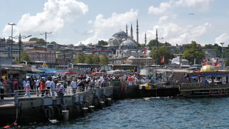 Escena-Típica-Del-Muelle-Lleno-De-Gente-En-Estambul,-Mezquita-Süleymaniye-En-Segundo-Plano