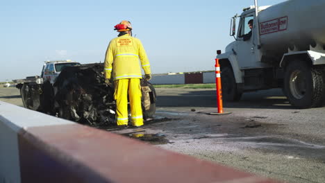 Firefighter-examining-the-severely-damaged-car-on-a-race-track-after-a-massive-fire-explosion