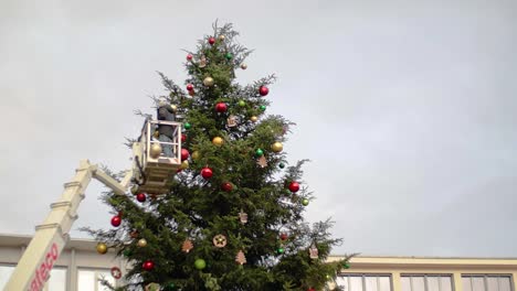 Two-workers-on-crane-decorating-big-Christmas-tree-in-public-city-square