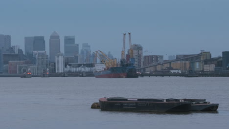 Pontón-En-El-Río-Támesis-Con-Barco,-Barrera-De-Mareas-Del-Támesis-Y-Muelle-Canario,-Paisaje-Urbano