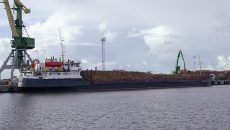 Frachtschiff-Voller-Holzstämme-Am-Hafenkran-Lädt-Holzstämme-Auf-Schiff,-Statisch,-Totale