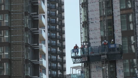 Ingenieros-Y-Trabajadores-De-La-Construcción,-En-Polipasto-Viajando-Por-Una-Torre-En-El-Sitio-De-Construcción