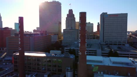 Backwards-Drone-shot-of-RJR-Tobacco-smoke-stacks-with-birds-flying-in-Winston-Salem,-NC