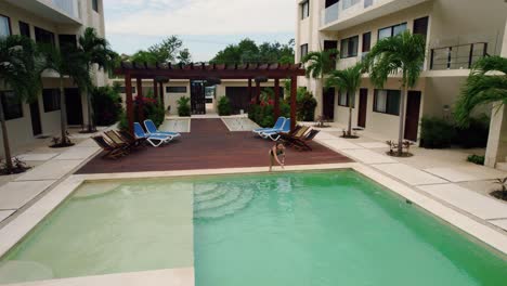 Drone-shot-of-a-girl-swimming-in-pool-at-the-Blue-Luxury-Hotel,-Tulum,-Mexico