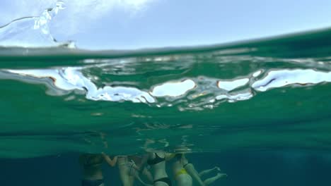 Anchored-boat-and-group-of-women-friends-swimming-in-blue-clean-transparent-ocean-seawater