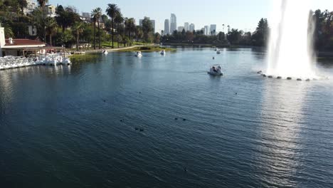 Vista-Aérea-De-Echo-Park-Y-Gente-En-Botes-De-Remo-En-El-Lago-Junto-A-Una-Fuente-Con-El-Centro-De-La-Ciudad-De-Fondo