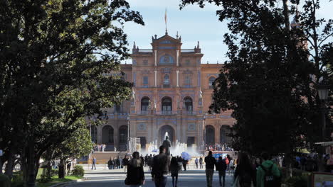 Gente-En-La-Plaza-De-España-Con-Fuente-De-Agua-Y-Edificio-Del-Instituto-Geográfico-Nacional-Al-Fondo-En-Sevilla,-España