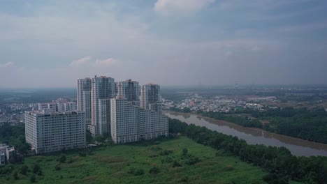 Volar-En-Toma-Aérea-A-Grandes-Bloques-De-Apartamentos-Modernos-A-Lo-Largo-Del-Río-Con-Zonas-Verdes-En-Los-Suburbios-Exteriores-De-La-Ciudad-De-Ho-Chii-Minh,-Vietnam