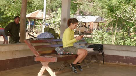 Joven-Asiática-Sentada-En-Un-Banco-De-La-Calle-Enviando-Mensajes-De-Texto-Con-Un-Teléfono-Inteligente