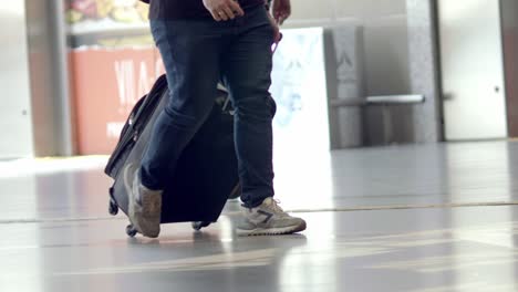 Toma-A-Nivel-Del-Suelo-De-Las-Piernas-De-Un-Viajero-Caminando-Por-El-Aeropuerto-Con-Un-Carrito-De-Equipaje