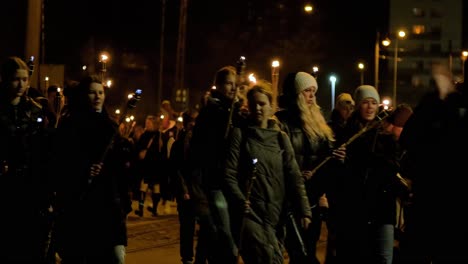 People-going-in-a-patriotic-torchlight-procession-in-Liepaja-city-on-Lacplesa-day-,-autumn-evening,-city-landscape,-traffic-lights,-medium-shot