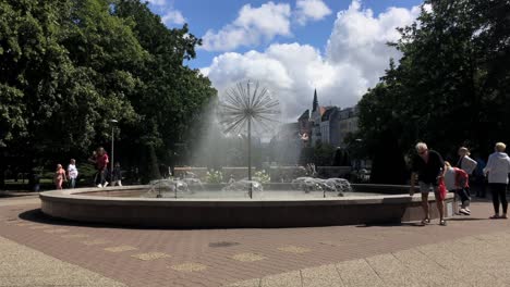 Fontanna-Dmuchawiec-in-Kolobrzeg,-Poland-with-people-relaxing-and-walking-around