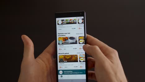 Male-hand-holding-and-scrolling-mobile-phone-with-Too-Good-To-Go-application-on-the-screen