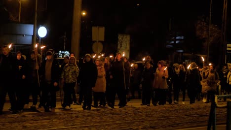 People-going-in-a-patriotic-torchlight-procession-in-Liepaja-city-on-Lacplesa-day-,-autumn-evening,-city-landscape,-traffic-lights,-wide-shot