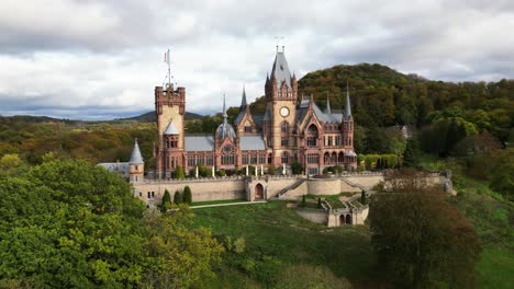 Toma-Panorámica-Del-Frente-Del-Castillo-De-Drachenburg-Situado-En-Drachenfels,-Königswinter,-Alemania-Con-Un-Hermoso-Sol-Otoñal-Y-Hojas-De-Colores