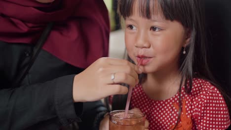 Mamá-Ayuda-A-Un-Niño-Asiático-A-Beber-Té-Helado-Dulce-En-El-Restaurante-Nasi-Jamblang-Plato-De-Arroz-Tradicional-Forma-Culinaria-Típica-Cirebon,-Java-Occidental,-Indonesia