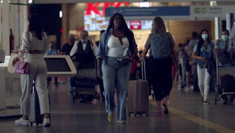 Toma-En-Cámara-Lenta-De-Viajeros-Caminando-Por-La-Concurrida-Sala-De-Salidas-Del-Aeropuerto-Con-Su-Equipaje