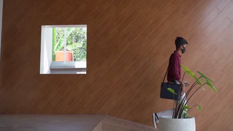 Indonesian-male-Business-Person-walk-come-out-of-the-cafe-dressed-business,-mask-and-carrying-a-bag-containing-a-laptop-with-a-wood-pattern-background-during-the-New-Normal-Pandemic-Covid-19