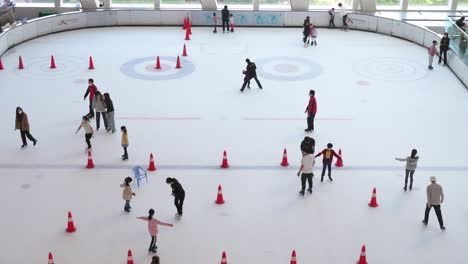 Vista-De-Pájaro-De-Participantes-Chinos-De-Todas-Las-Edades-Vistos-Disfrutando-Y-Aprendiendo-Patinaje-Sobre-Hielo-Bajo-Techo-En-Un-Centro-Comercial-En-Hong-Kong