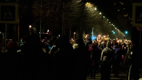 Personas-Que-Van-En-Una-Procesión-Patriótica-De-Antorchas-En-La-Ciudad-De-Liepaja-El-Día-De-Lacplesa,-Tarde-De-Otoño,-Paisaje-De-La-Ciudad,-Semáforos,-Plano-General