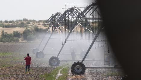 Arbeiter,-Die-Neben-Einer-Zentralen-Bewässerungs-Sprinkleranlage-Stehen,-Die-Landwirtschaftliche-Feldfrüchte-In-Punjab-Bewässert