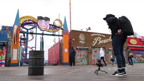 Hooded-Freelance-Filmmaker-Setting-Up-Camera-On-Floor-Outside-Entrance-To-Coney-Island