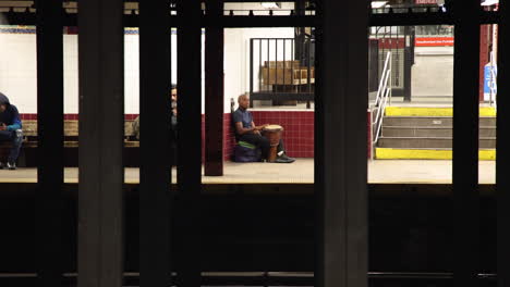 Músico-Callejero-Masculino-Tocando-El-Tambor-En-La-Estación-De-Nueva-York-Visto-Desde-El-Otro-Lado-De-La-Plataforma