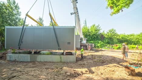 Crane-and-work-team-lifting-and-placing-a-placing-a-construction-site-trailer-office-on-its-foundation---time-lapse