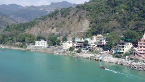 Antiguo-Templo-Hindú-En-La-Orilla-Del-Río-Ganges-Con-Un-Puente-De-Hierro-Que-Conduce-La-Línea-En-El-Día-Desde-Un-Video-De-ángulo-Plano-Tomado-En-El-Templo-Trimbakeshwar-Lakshman-Jhula-Rishikesh-Uttrakhand-India-El-15-De-Marzo-De-2022