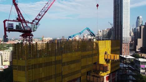 Aerial-view-of-a-building-under-construction-and-the-Brooklyn-skyline,-in-sunny-NYC---Ascending,-drone-shot