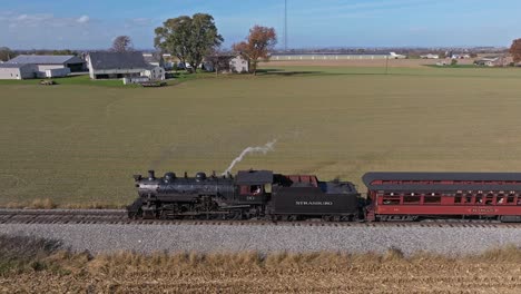 Eine-Parallele-Luftaufnahme-Eines-Dampfpersonenzuges-Auf-Einer-Eingleisigen-Strecke-Durch-Ackerland-An-Einem-Sonnigen-Tag