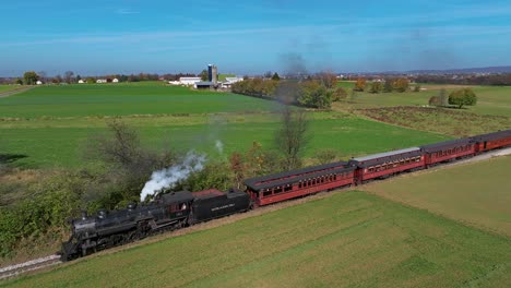 Eine-Luftaufnahme-Eines-Dampfzuges,-Der-Rauch-Bläst,-Während-Er-An-Einem-Sonnigen-Herbsttag-Durch-Landwirtschaftliche-Flächen-Fährt