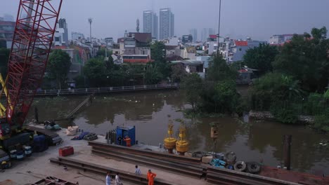 Aerial-fly-out-to-reveal-dredging-equipment-and-workers-on-a-barge-on-the-Saigon-River-in-Ho-Chi-Minh-City,-It's-a-sunny-day-with-blue-sky-but-with-very-high-air-pollution