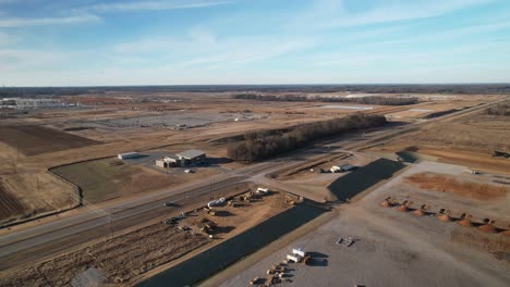 Aerial-approach,-descending-towards-cars-travelling-on-highway-with-sprawling-new-construction-in-background