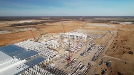 Aerial-orbital-zoom-out-of-steel-structure-under-construction-surrounded-by-heavy-machinery-and-cranes