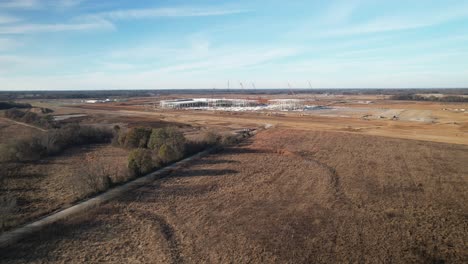 Aproximación-Aérea,-Panorámica,-Alrededor-De-Una-Gran-Estructura-De-Acero-En-Construcción-Rodeada-De-Grúas,-Equipo-De-Construcción-Y-Tierra-Nivelada