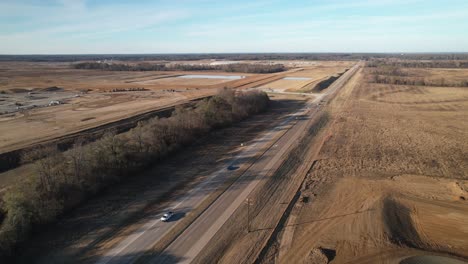 Slow-aerial-zoom-out-of-sprawling-new-construction-adjacent-to-cars-travelling-on-highway